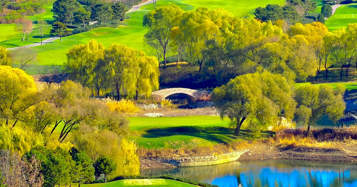Aerial view of a golf course with rolling fairways, a stone bridge, and water features