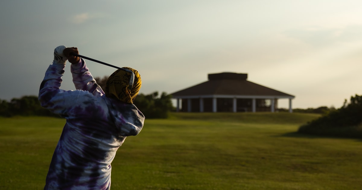 A golfer swinging toward the clubhouse green at dusk