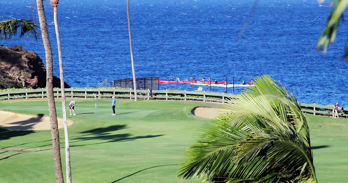 An oceanside golf course green with palm trees and blue water